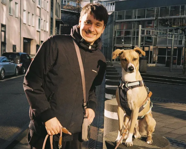 Ein Foto von Manuel, wie er mit dem Hund vor einem Gebäude steht.